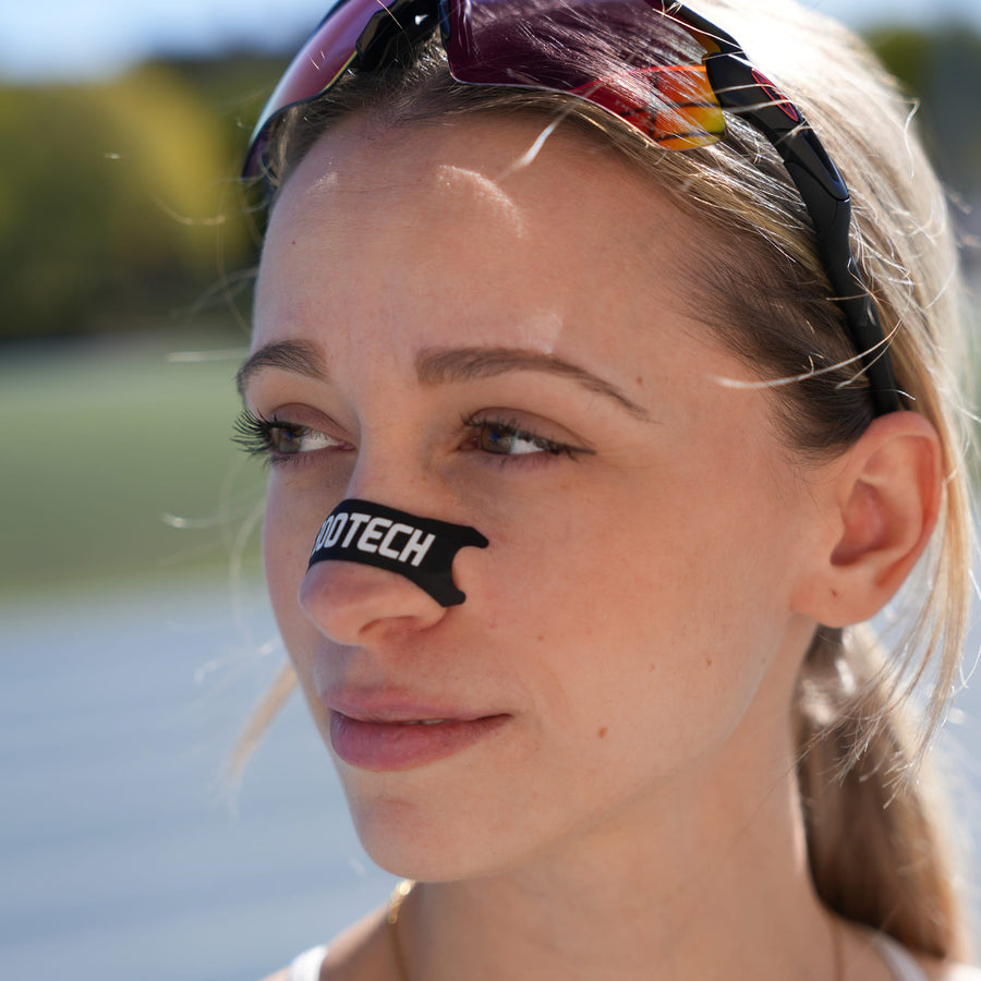 Mujer deportista con tiras nasales BOOTECH negras y gafas de sol, recuperación deportiva.