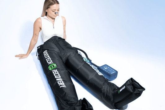 Deportista descansando en el suelo mientras utiliza botas de presoterapia en sus piernas tras entrenar.