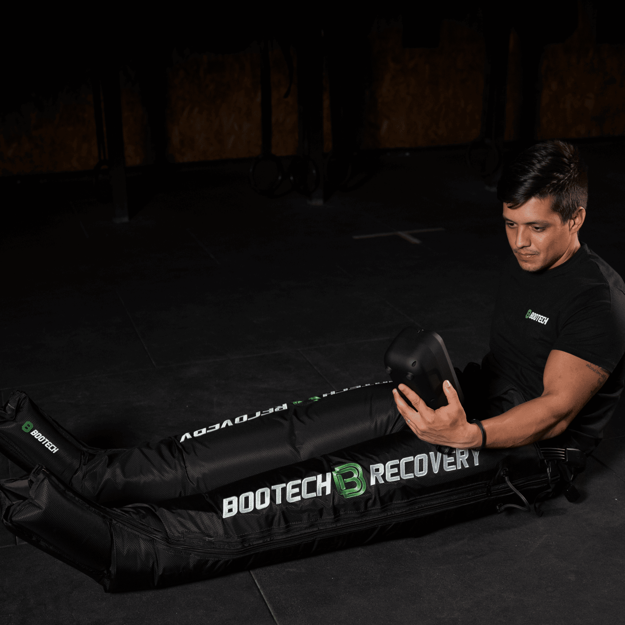 Hombre usando presoterapia BOOTECH para recuperación deportiva en gimnasio oscuro